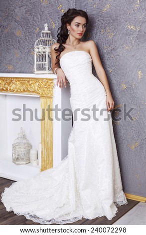 fashion interior photo of beautiful young bride with dark hair in elegant wedding dress posing in luxurious studio