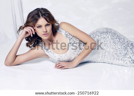 fashion photo of beautiful model in luxurious silver dress posing in white studio