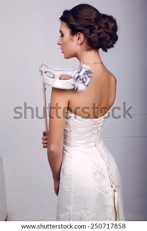 fashion photo of beautiful elegant bride in wedding dress with mask in her hands, posing in  studio