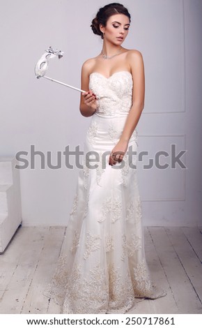 fashion photo of beautiful elegant bride in wedding dress with mask in her hands, posing in  studio