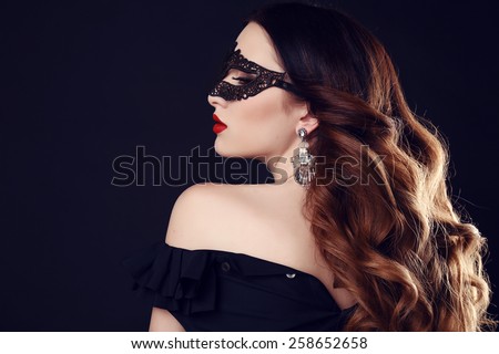 fashion photo of gorgeous woman with dark hair and blue eyes, with lace mask on her face,posing in dark studio