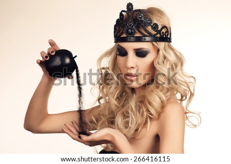 fashion studio portrait of sexy beautiful woman with long blond hair and bright makeup,looking like a witch, holding black magic apple in hands