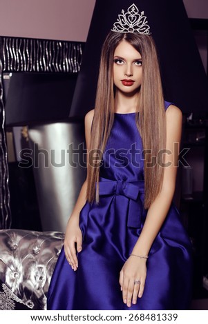 fashion photo of gorgeous woman with dark hair  in elegant dress and crown posing in luxurious interior