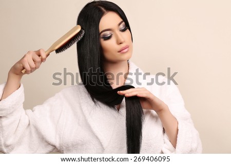 fashion studio photo of beautiful sensual woman combing her luxurious straight hair, wearing white cozy bathrobe