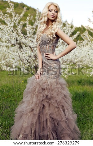 fashion outdoor photo of beautiful sensual woman with long blond hair in luxurious sequin dress posing in spring blossom garden