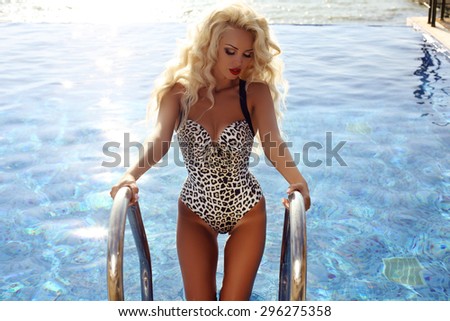 fashion outdoor photo of gorgeous sexy woman with blond hair in elegant swimsuit relaxing beside swimming pool