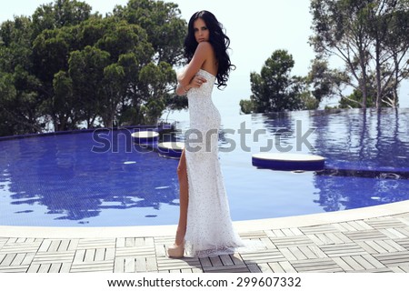 fashion outdoor photo of beautiful sensual woman with long dark hair in luxurious sequin dress posing in swimming pool