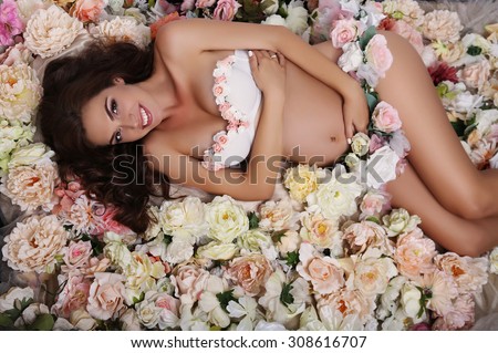 fashion studio photo of beautiful pregnant woman with dark hair lying among rose flowers
