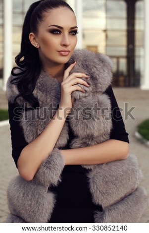 fashion outdoor photo of gorgeous woman with long dark hair wears luxurious fur coat, posing on street