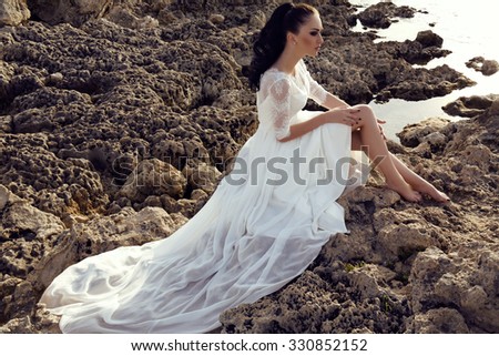 fashion outdoor photo of gorgeous young woman with long dark hair in luxurious lace wedding dress,dreaming on the sea coast