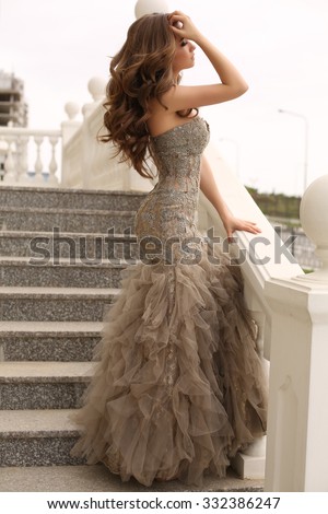fashion outdoor photo of beautiful sensual woman with long dark hair in luxurious sequin dress posing on stairs
