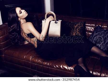fashion interior photo of beautiful woman with dark curly hair and evening makeup,wears elegant dress, holding bag in hands