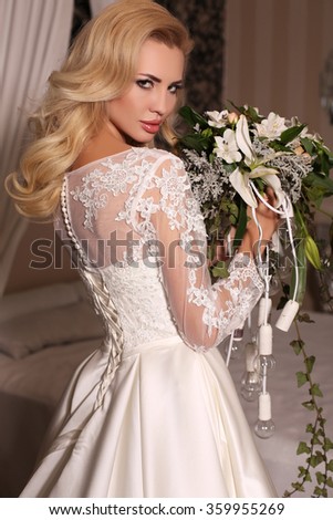 fashion studio photo of gorgeous bride with blond hair, in luxurious wedding dress with bijou, holding bouquet of flowers