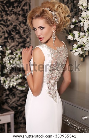 fashion studio photo of gorgeous bride with blond hair, in luxurious wedding dress with bijou, posing in decorated room
