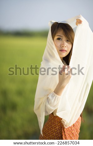 Thai woman wearing Thai style costume shading her face with thin cloth in rice field in Thailand