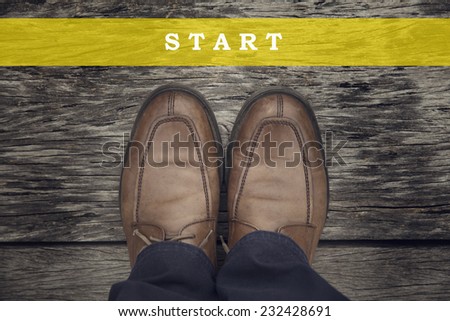 A business man is looking down at his feet with a  yellow race line that says start here