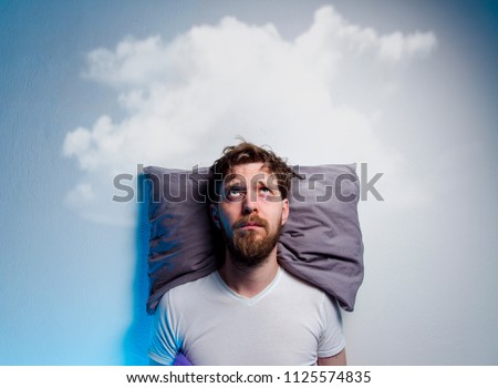 Man having problems/ insomnia, laying in bed on pillow, looking up to gray cloud over his head, copy space