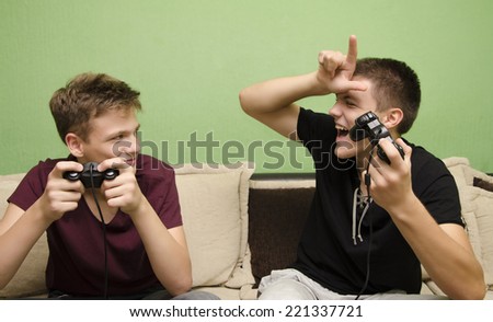 Teenage boy teasing younger brother with loser sign while playing video game