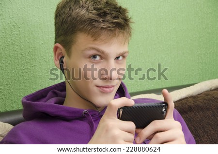 Beautiful blue-eyed teenager listening to music on smart phone, looking at camera. Selective focus on the eyes