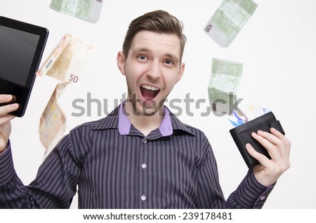 Young adult man holding tablet and credit cards, while money (euros) is falling from air, earning money online concept. Shopping online concept. Online banking