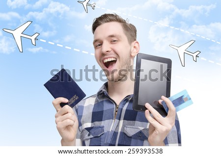 Young man traveling concept, smiling while holding tablet, passport and credit cards, booking flights via tablet online and traveling around the world. Graphic planes in background