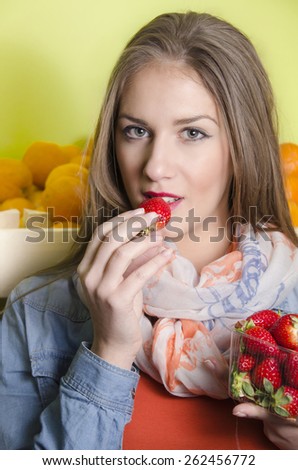 Beautiful natural looking brunette girl posing in fruit market, while eating strawberries