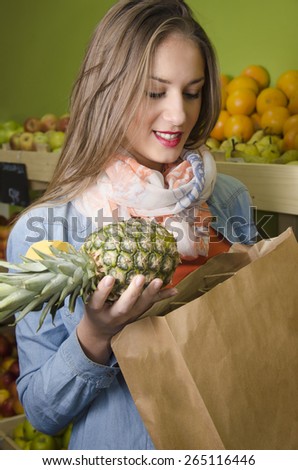 Beautiful girl buying pineapple, putting it in a paper bag, healthy lifestyle