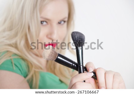 Girl holding crossed makeup brushes, implies that makeup is bad for skin, wearing only lipstick. Selective focus on brushes