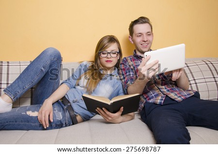 Couple spending free time together, girl reading a book, while her boyfriend is using tablet. Selective focus on girl