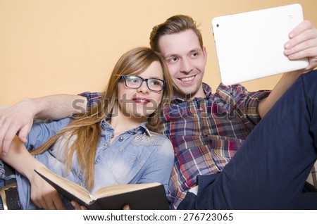 Boyfriend and girlfriend relaxing together on a couch, young man showing his girlfriend something on tablet, while she holds a book. Selective focus on girl