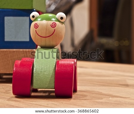 Green car toy with big red wheels on a wooden table, a big smile and wide white eyes