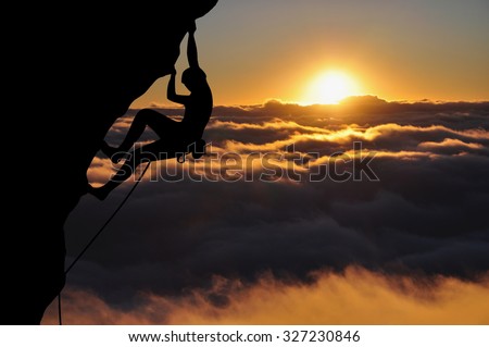 Climber silhouette high above clouds and mountains. Young woman climbing top rope during sunset.