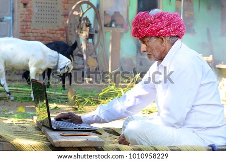 Indian Villager works on laptop at his farm with livestock(goats) in Background. Reach of technology in India. Indian farmer uses technology to work from home. Scope of Technology in Rural India.