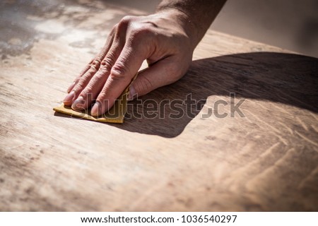 Gritty weathered man\'s hand and sandpaper; hand sanding a table top to refinish with paint or stain