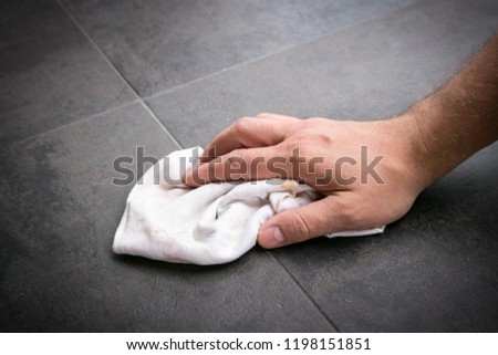 Man\'s hand wipes clean rag across freshly installed vinyl flooring tiles.