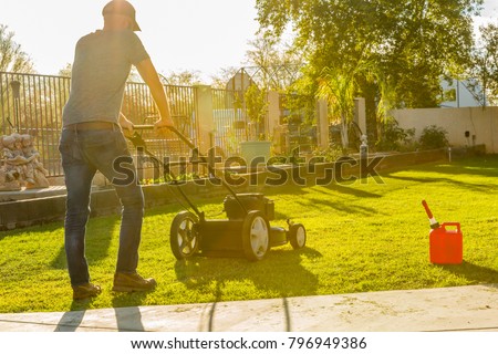 Man mowing lawn with push mower at miday, gas tank near by.