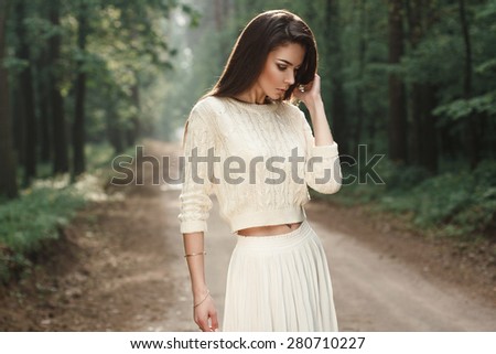 Portrait of a pretty woman in a white sweater on the road in the forest with fog.