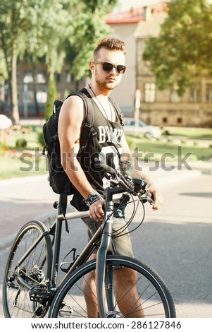 Portrait of a young man with a bicycle on the street. Black T-shirt with print 23