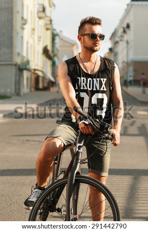 Young hipster man with bicycle sitting on a bicycle in the city. Black T-shirt with print 23