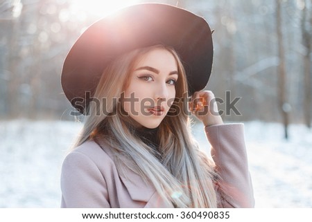 Portrait of a young beautiful girl in a black hat on a winter day at sunset