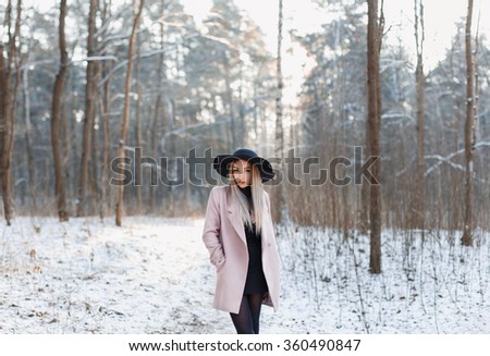 Pretty fashionable woman in black hat and pink coat in winter amazing woods at sunset