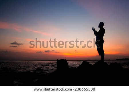 silhouette of man standing on the rocky beach during sunset, praying