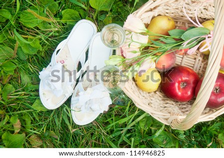 Picnic background of basket with fruits and flowers, shoes lying on the grass