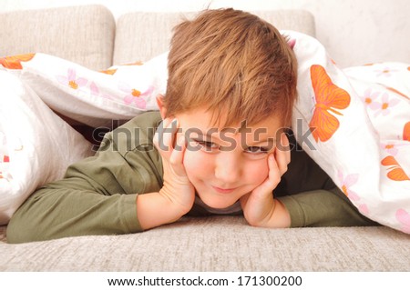 Smiling child lying in the bed under blanket