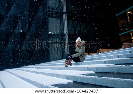 Young woman sitting on the stairs and watching snow falling