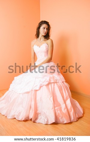 Beautiful bride in a wedding dress sitting on the chair in the peach color room