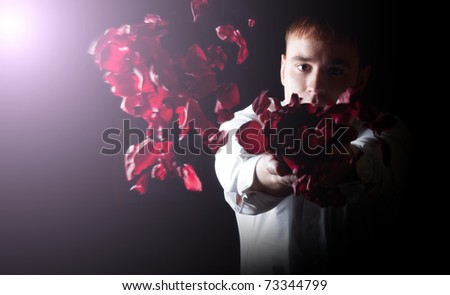 Young handsome man throwing rose petals, on black background