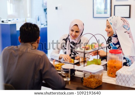 A Muslim family sits down for a meal at home. Two women in head scarves and a man enjoy a quiet repast.
