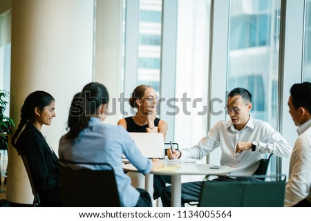 A diverse team of business people have a productive and efficient meeting. They are sitting around each other at a table and having an animated discussion. Some of them are smiling while others think.