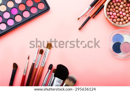 Various makeup products on pink background with copy space